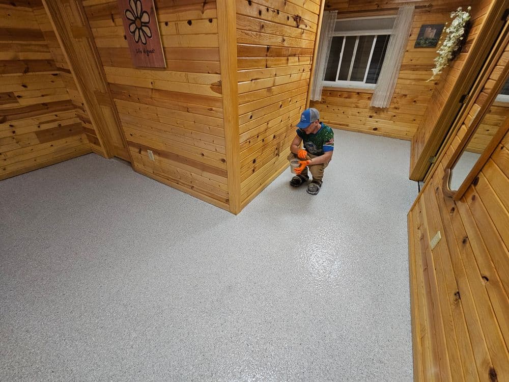 Child applying a colorful sealant on a freshly finished gray epoxy floor in a wooden interior.