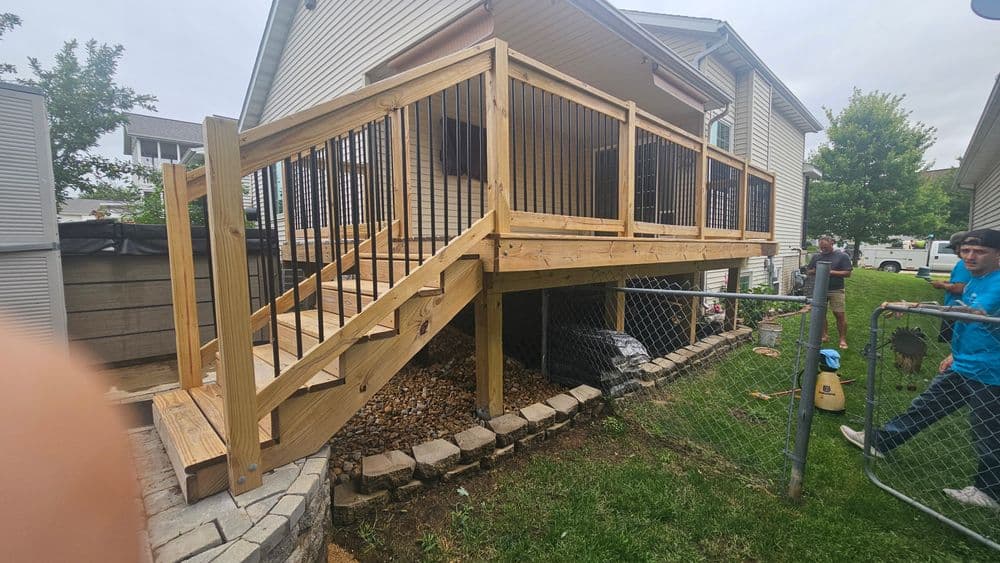 Newly built wooden deck with staircase, surrounded by grass and stone pathway. Family backyard setting.