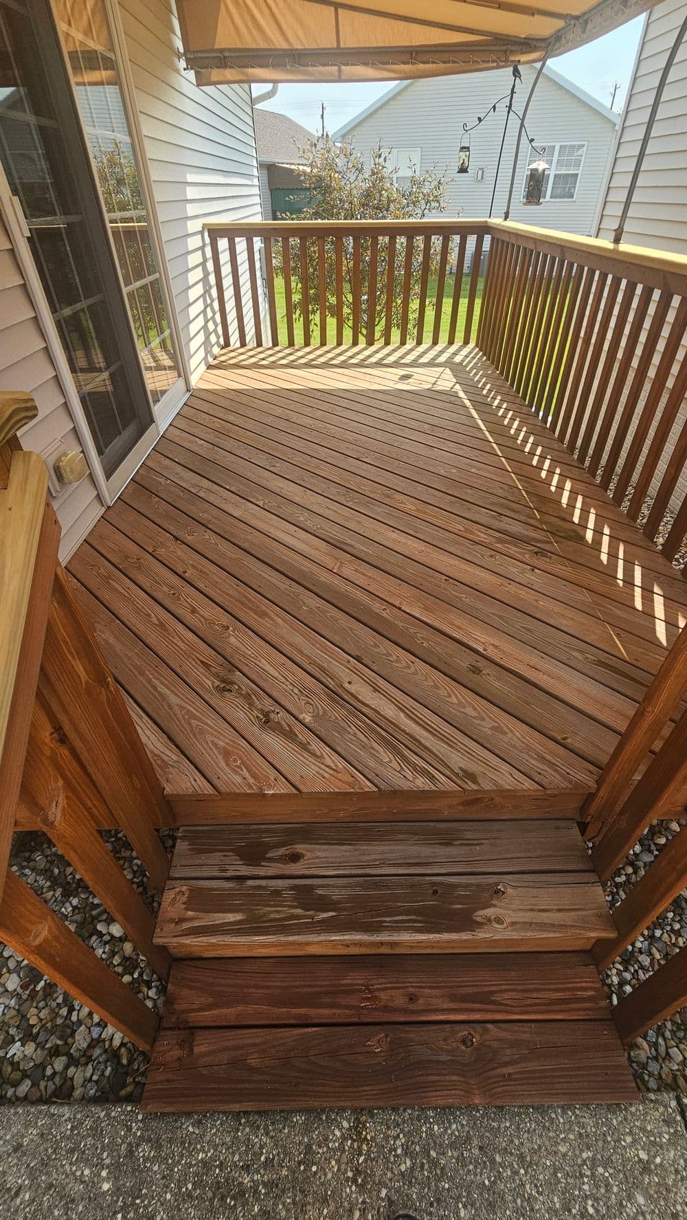 Well-maintained wooden deck with railing and steps, surrounded by a residential yard.
