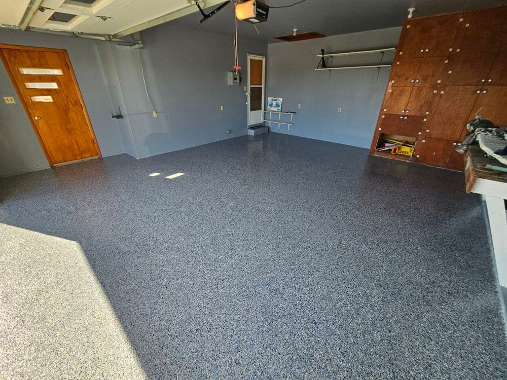 Spacious garage with epoxy flooring, gray walls, wooden door, and organized shelves.