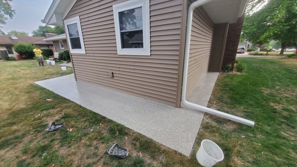 Home exterior with newly finished concrete patio beside brown siding and grass lawn.