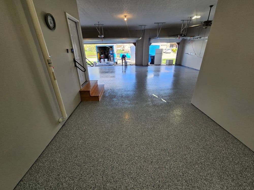 Finished garage with shiny epoxy floor, garage doors open, and person unloading a truck.
