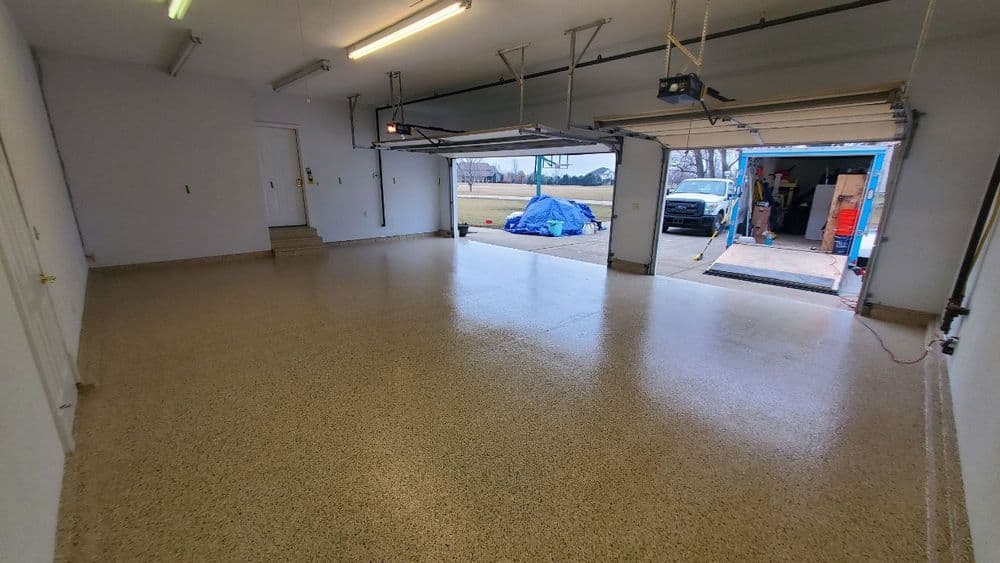 Spacious empty garage with polished floor, open doors, and vehicles outside.