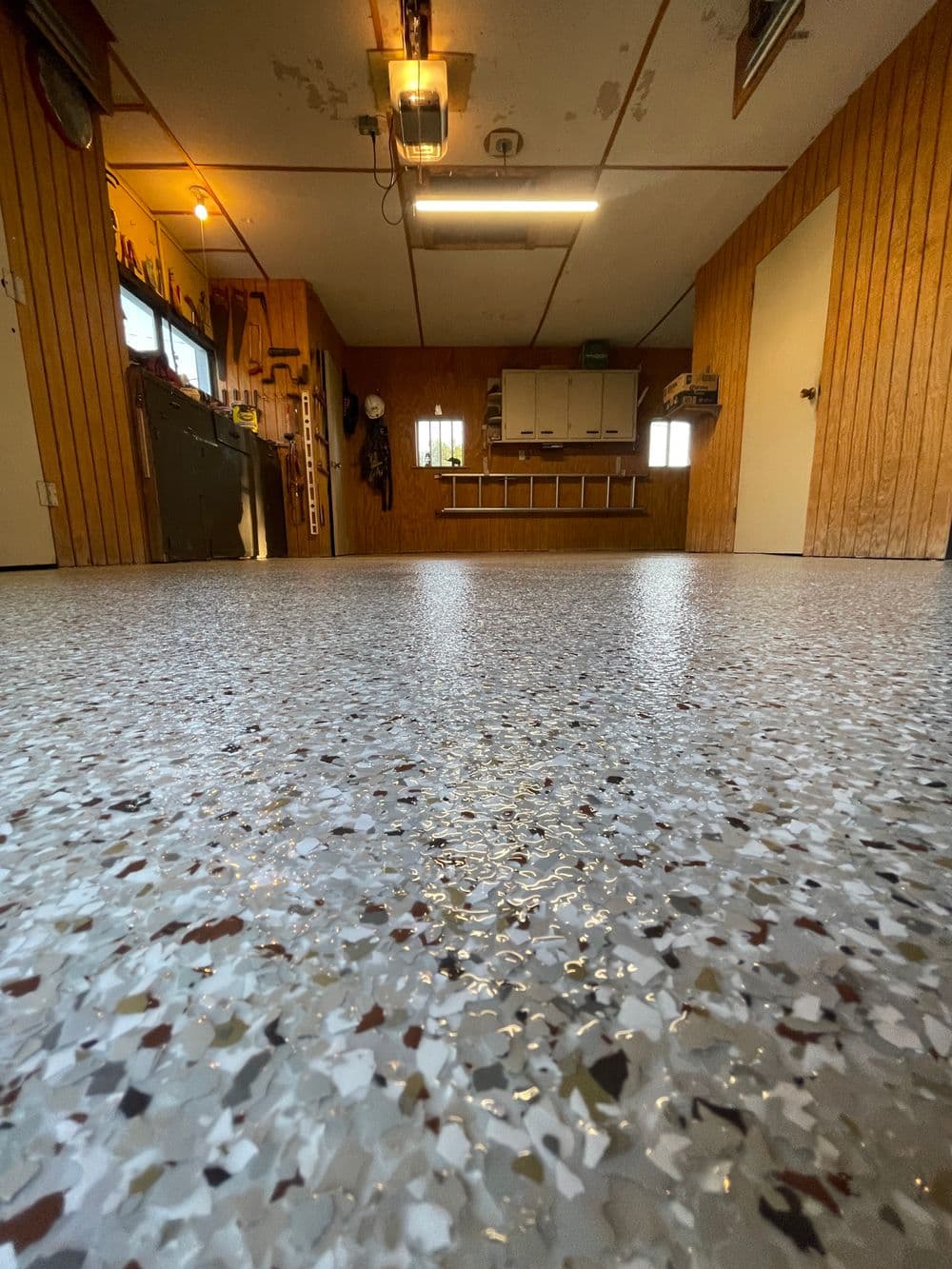 View of a polished garage floor with speckled epoxy finish and wooden panel walls.