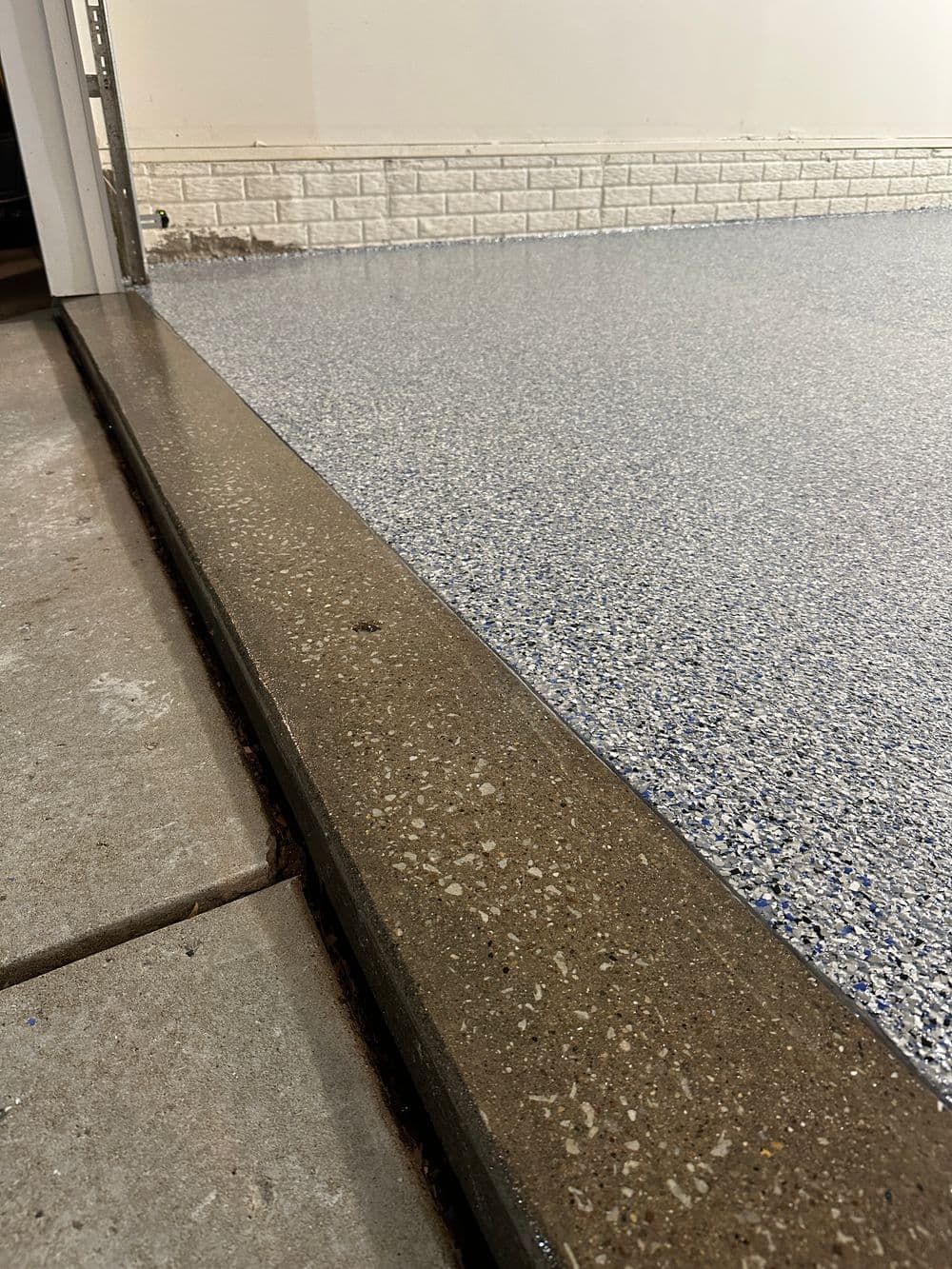 Textured epoxy garage floor with a smooth concrete edge and light-colored wall.