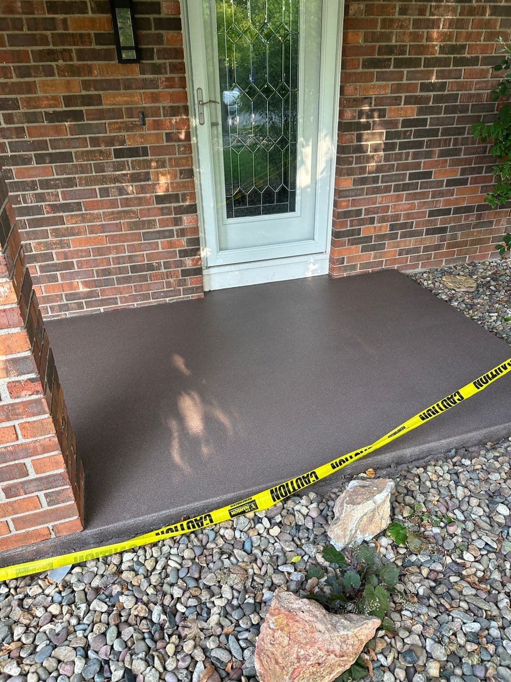Newly poured concrete porch with caution tape, featuring a brick façade and landscaping stones.