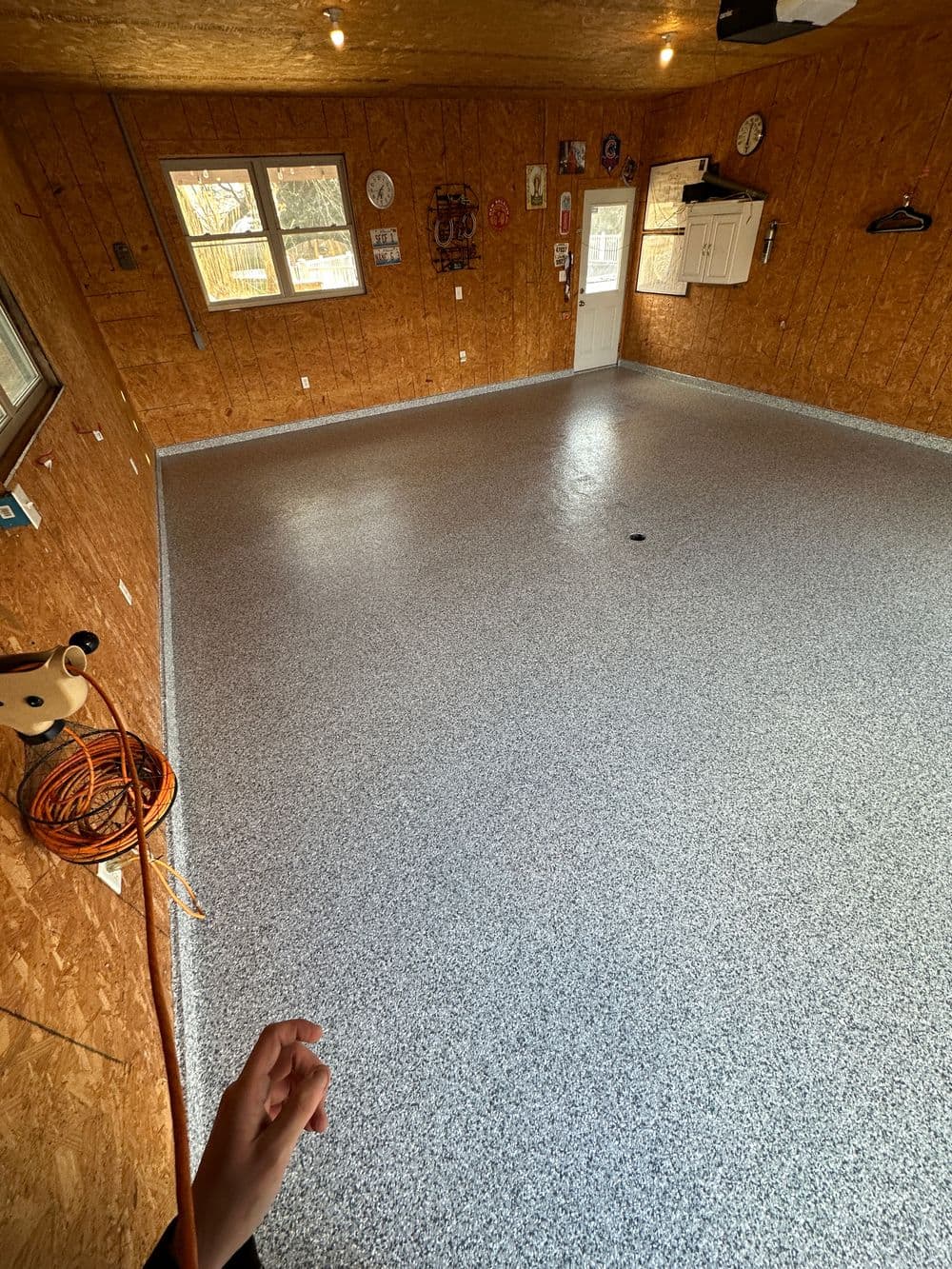 Spacious garage interior with gray epoxy floor, wood paneling, and natural light from windows.