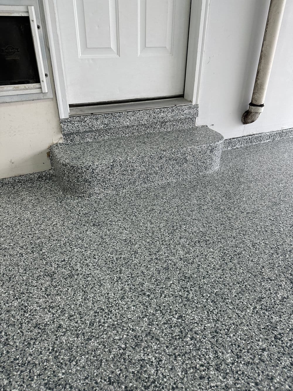 Entryway with gray patterned epoxy flooring and steps leading to a white door.