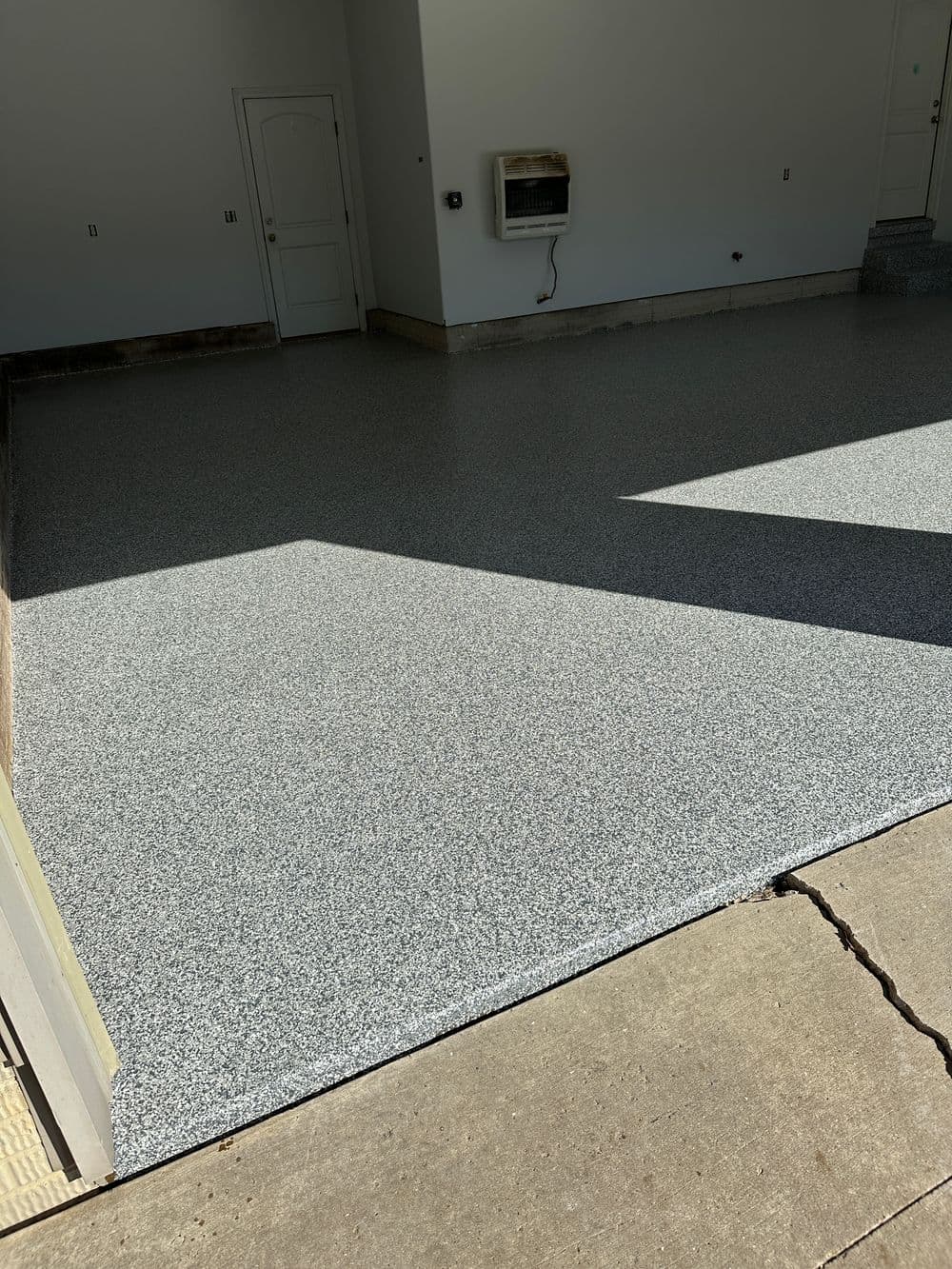 Newly coated garage floor with gray speckled finish and clean entrance.