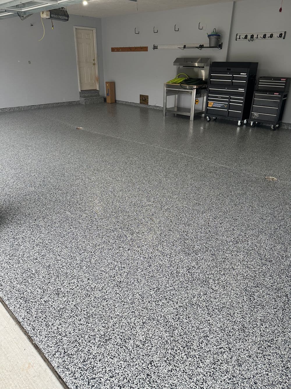 Newly coated garage floor with gray speckled epoxy finish and organized tool storage.