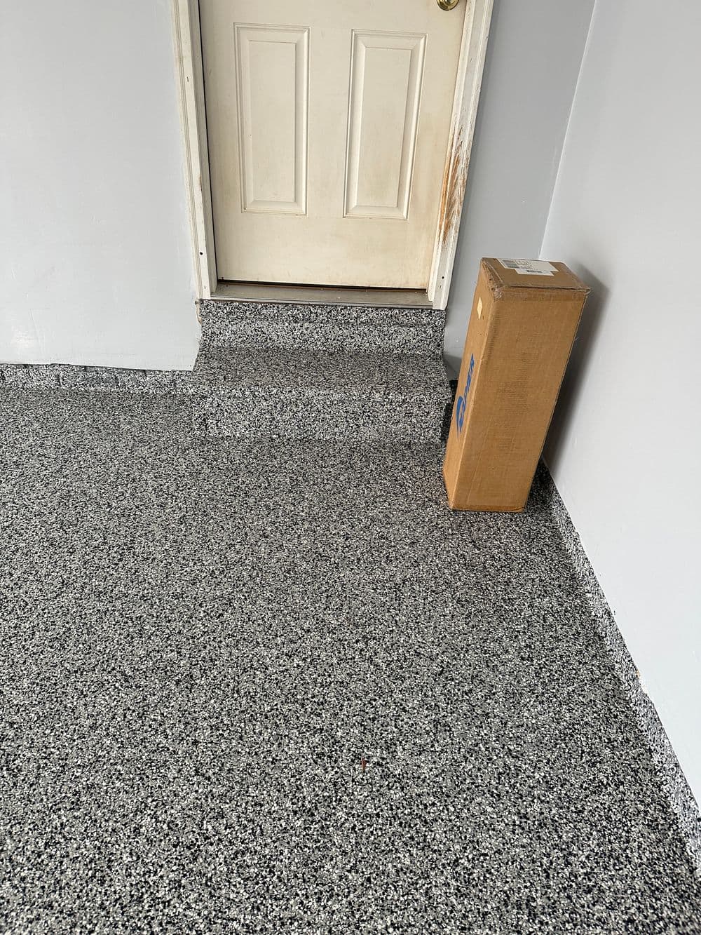 Delivery box beside a door on a textured gray floor.