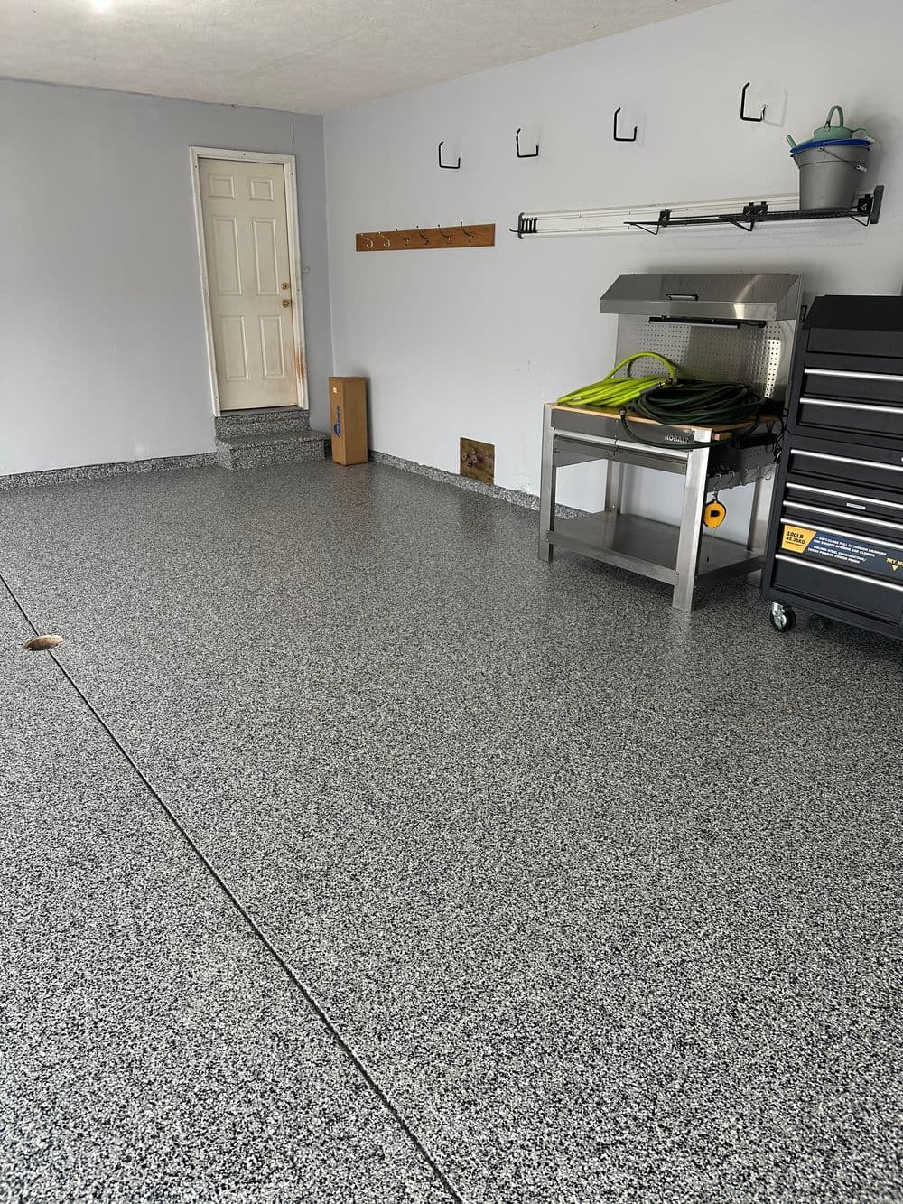 Clean garage interior with epoxy flooring, metal shelving unit, and wall hooks.