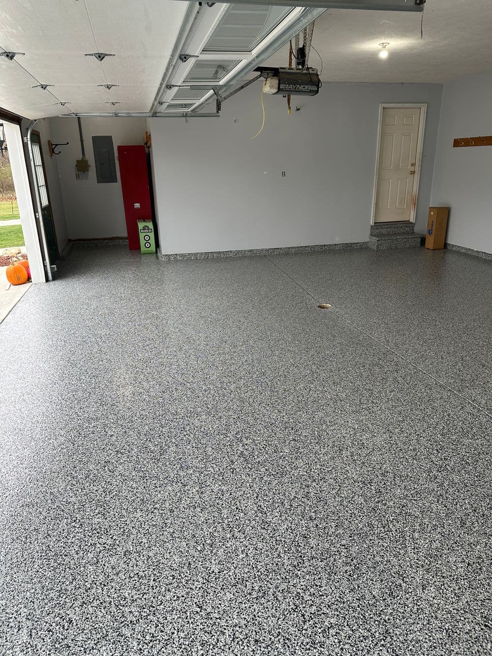 Clean, spacious garage with gray epoxy floor, white walls, and wooden storage shelf.