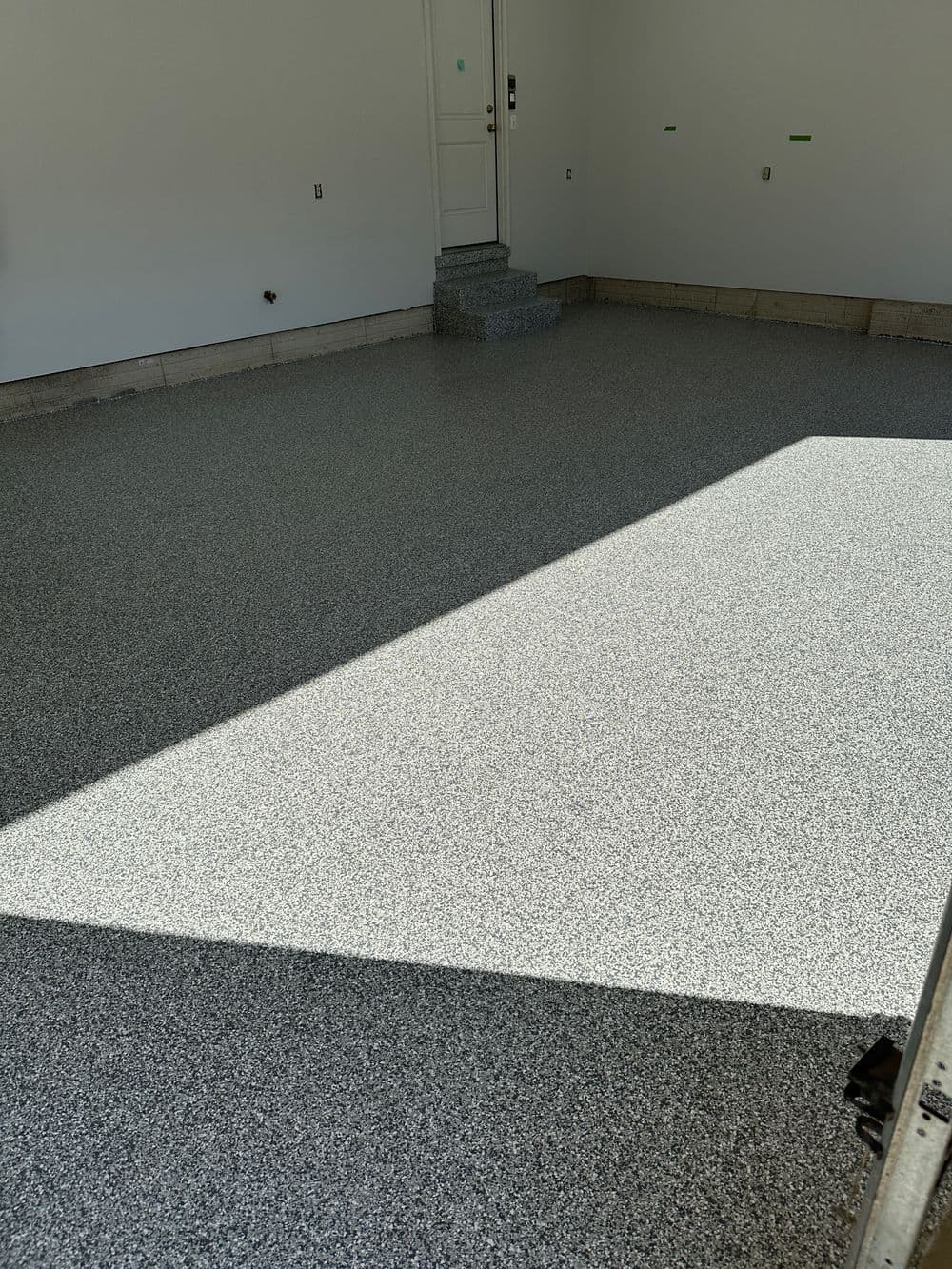Newly installed epoxy garage floor with gray speckled finish and clean, empty space.
