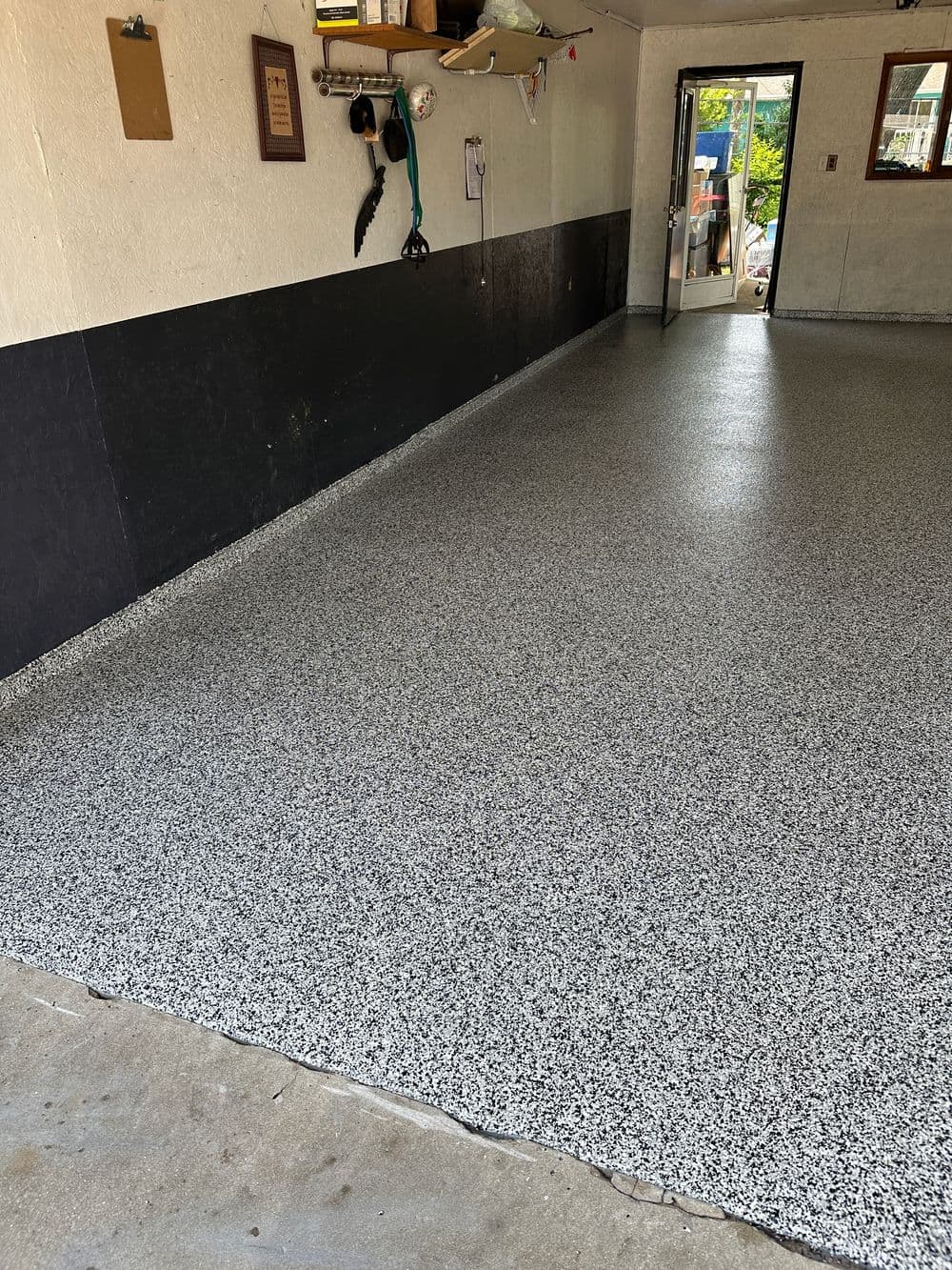 Newly coated garage floor with a black and grey speckled epoxy finish, door open to outside.